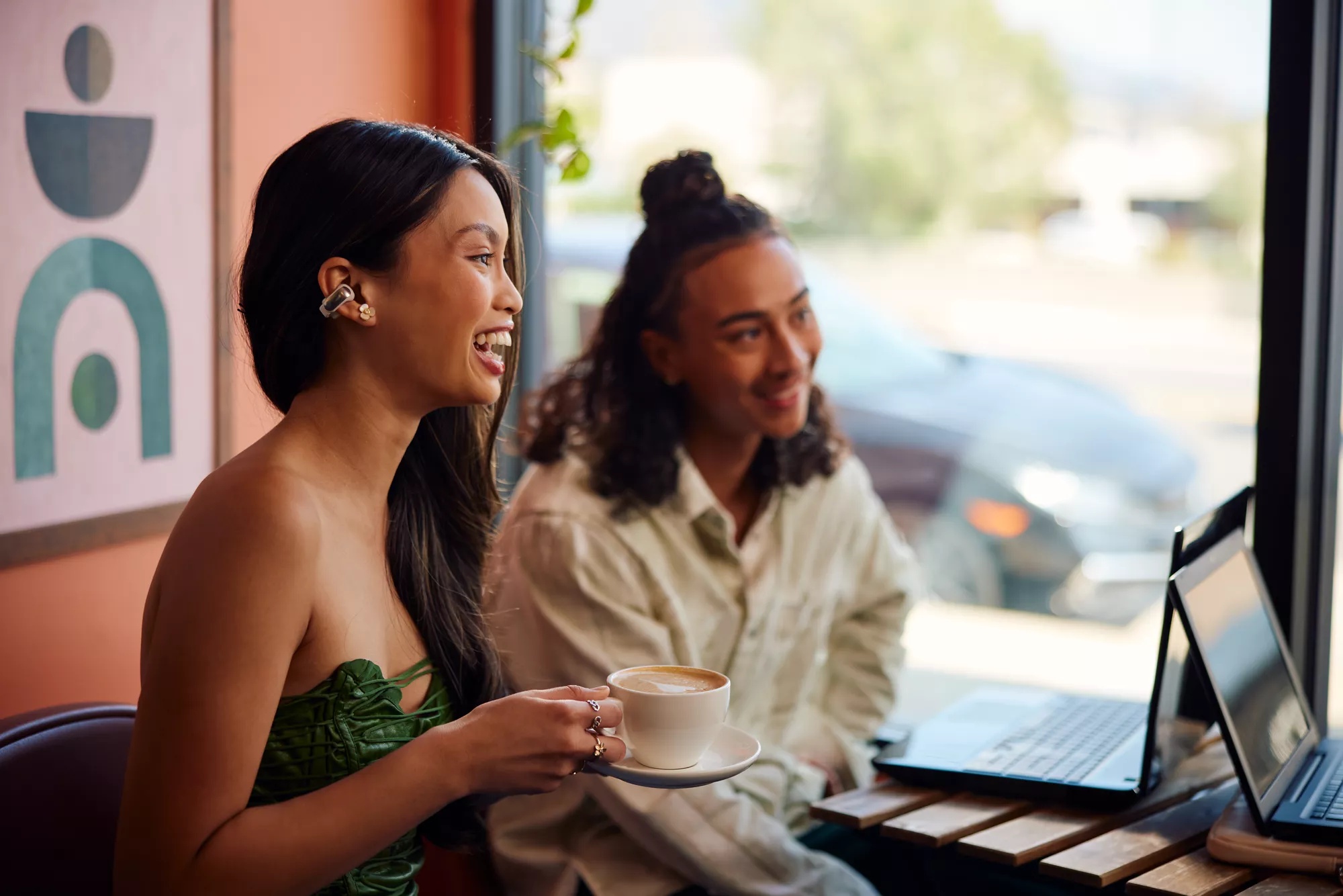 Femme portant des écouteurs oreilles libres Bose Ultra dans un café, tout en buvant un café avec des amis.