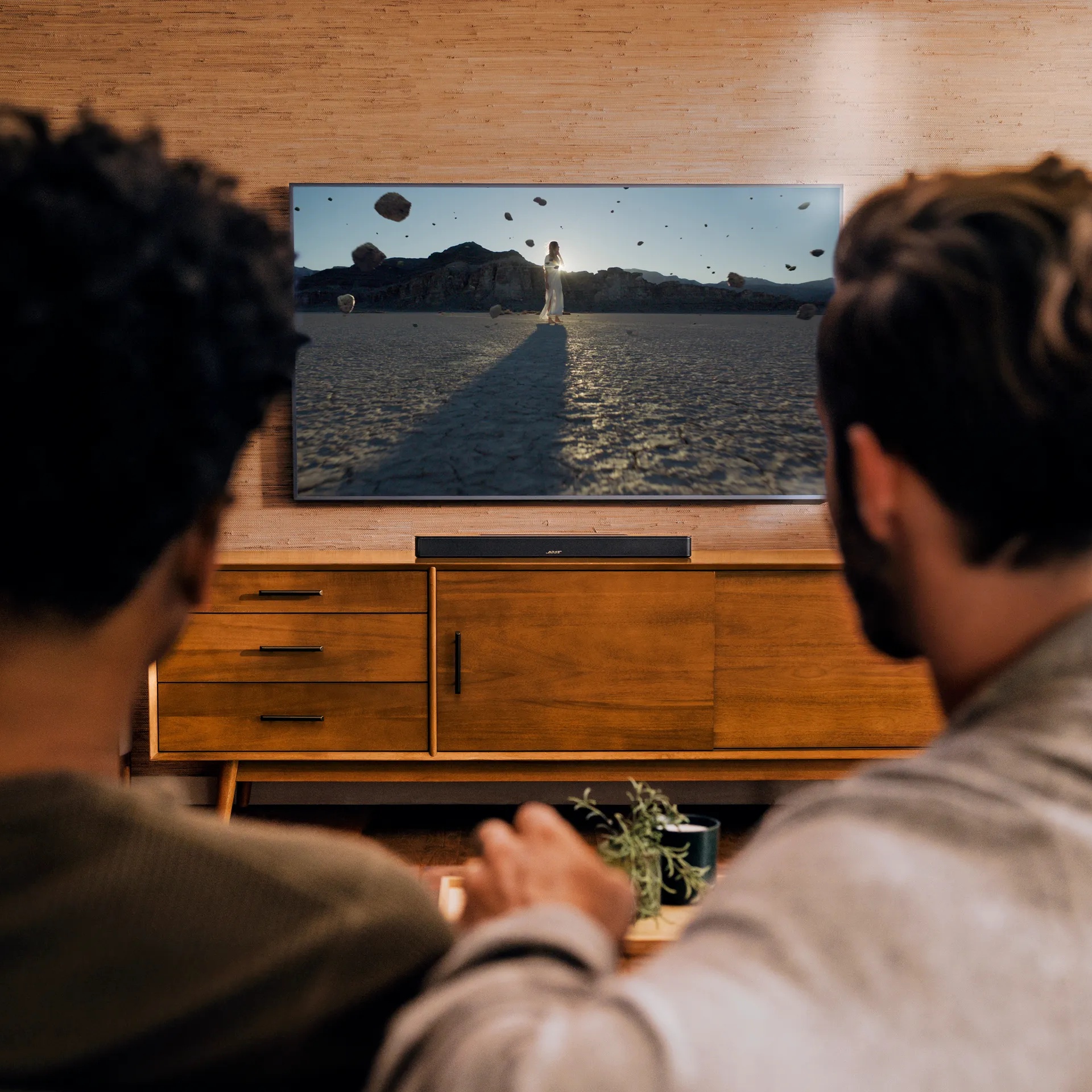 Friends watching TV with a Bose Smart Soundbar on a TV console.